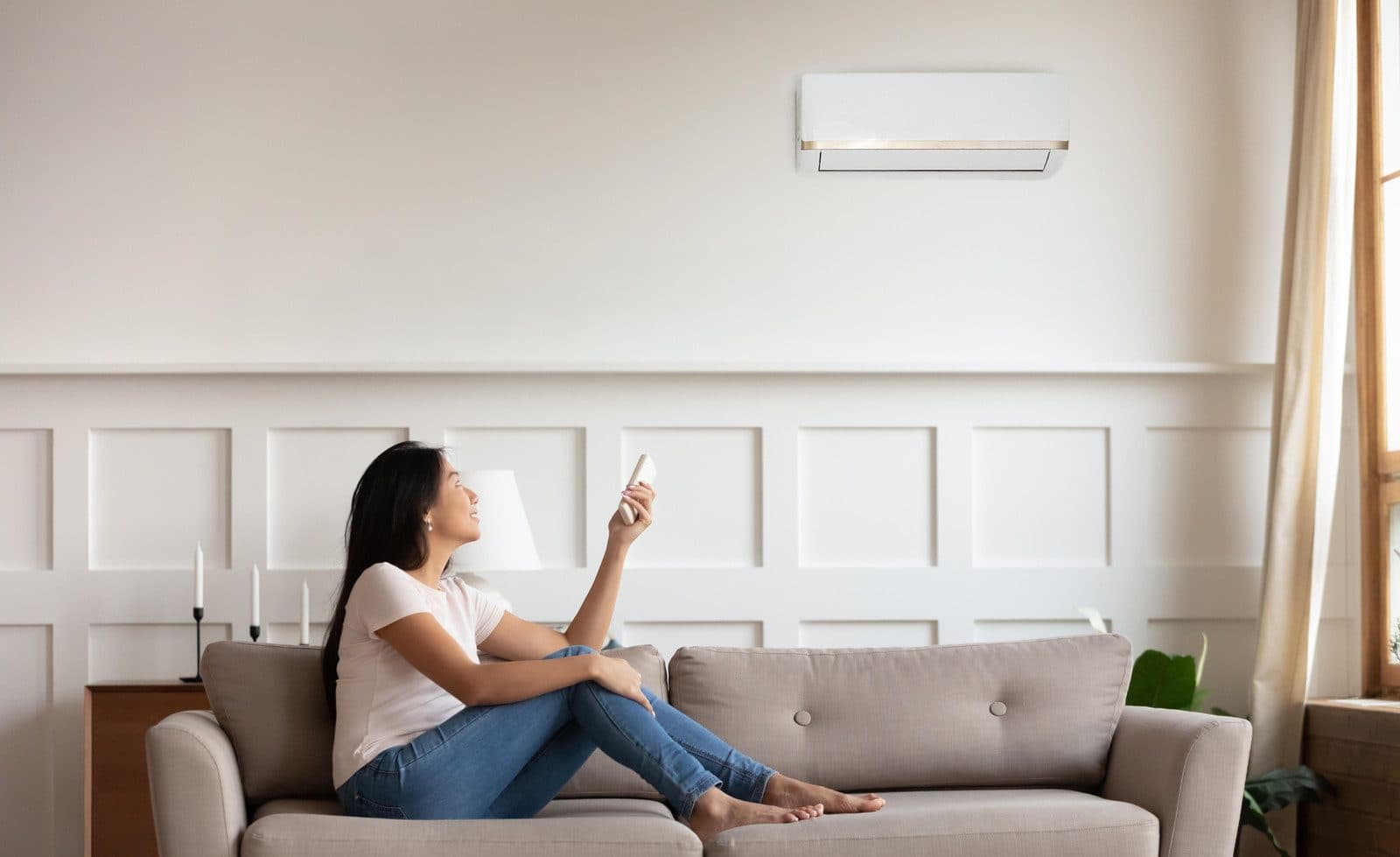 Woman relaxing on a sofa, adjusting a wall-mounted split system with a remote control